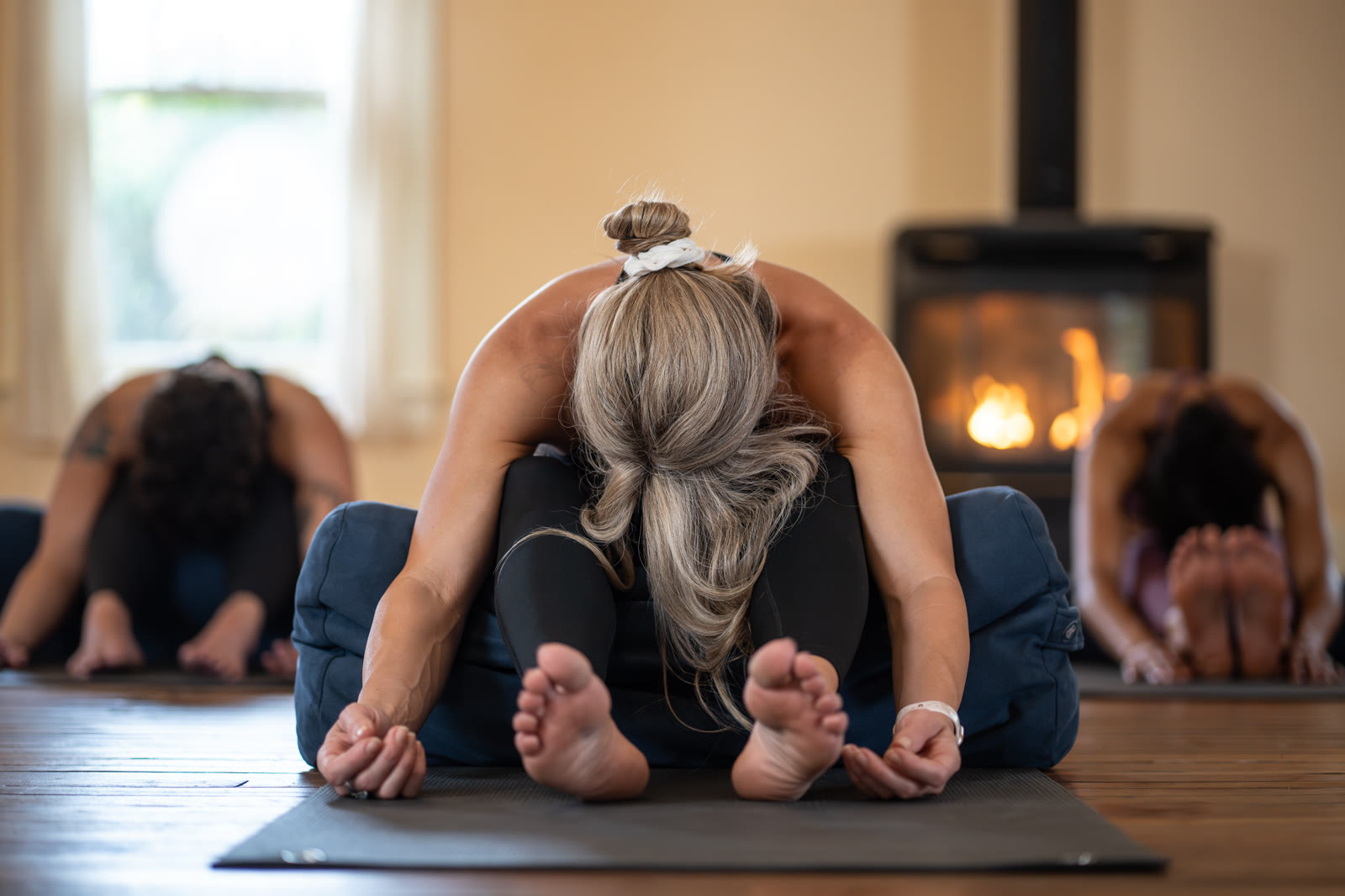 Students folding forward on their mats beside the fireplace in the warm studio