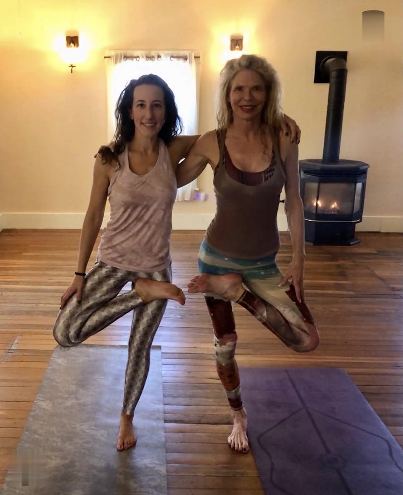 Two teachers in tree pose by the fire